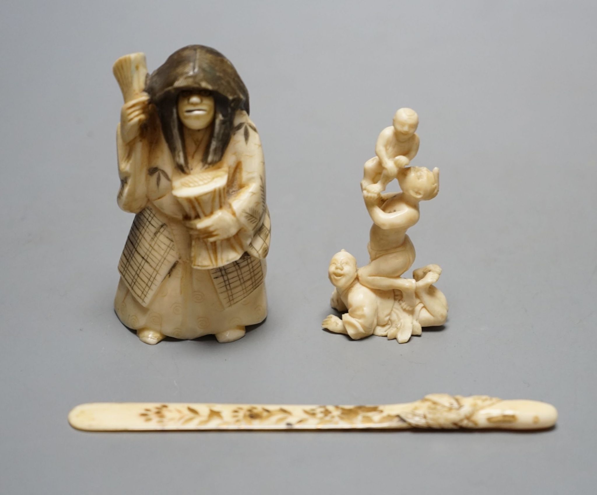 A Japanese face changer, early 20th century, a small okimono of acrobats, Meiji period and an ivory paper knife with lacquer decoration, face changer 8 cms high.